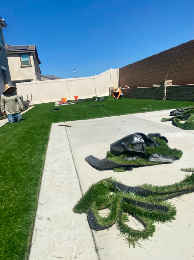 Crew rolling out artificial turf on a front yard in Perris, CA