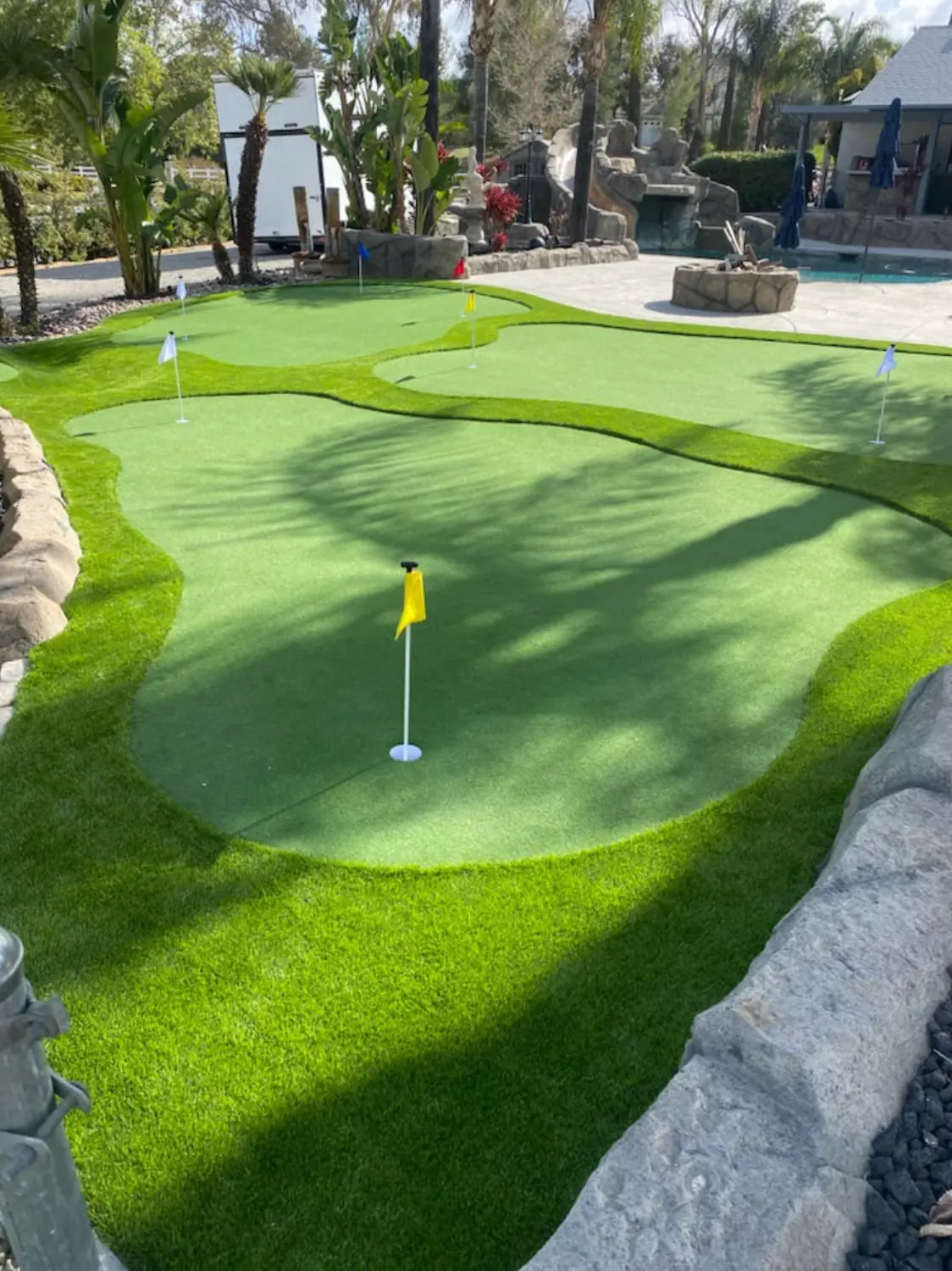 Backyard putting green with a yellow flag and rock border in Perris, CA